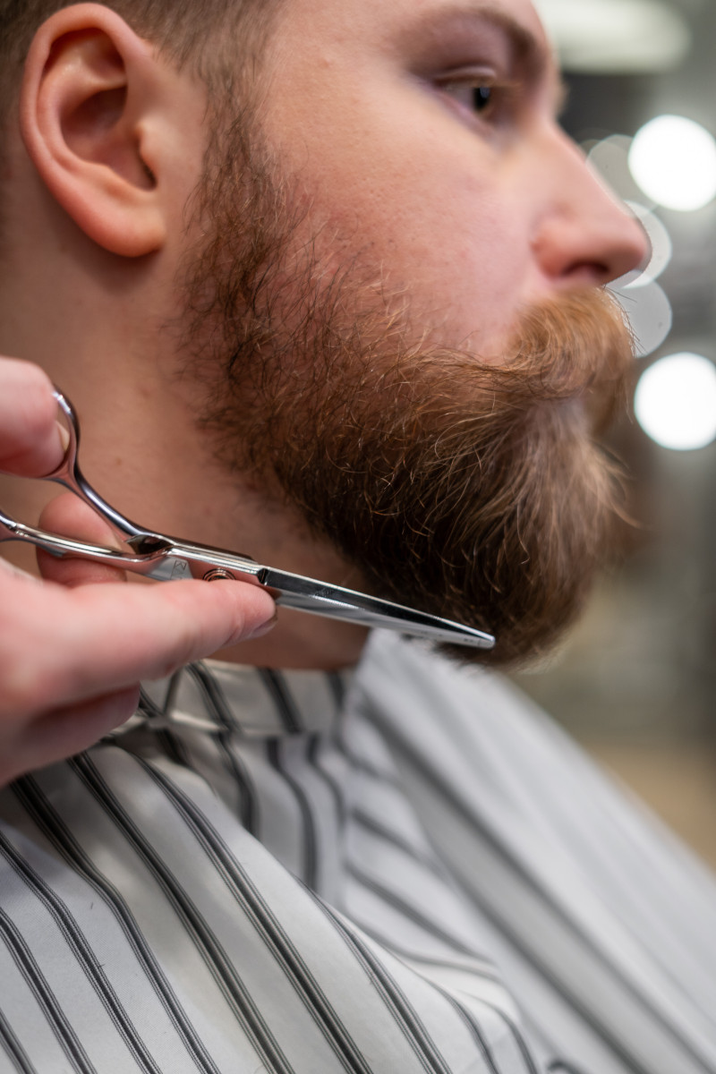 Man having his beard trimmed by a stylist with scissors